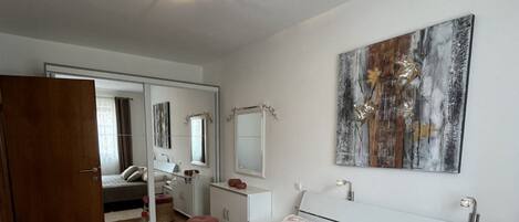 A bedroom with a bed, a bedside table, a mirror, and a large abstract painting on the wall.