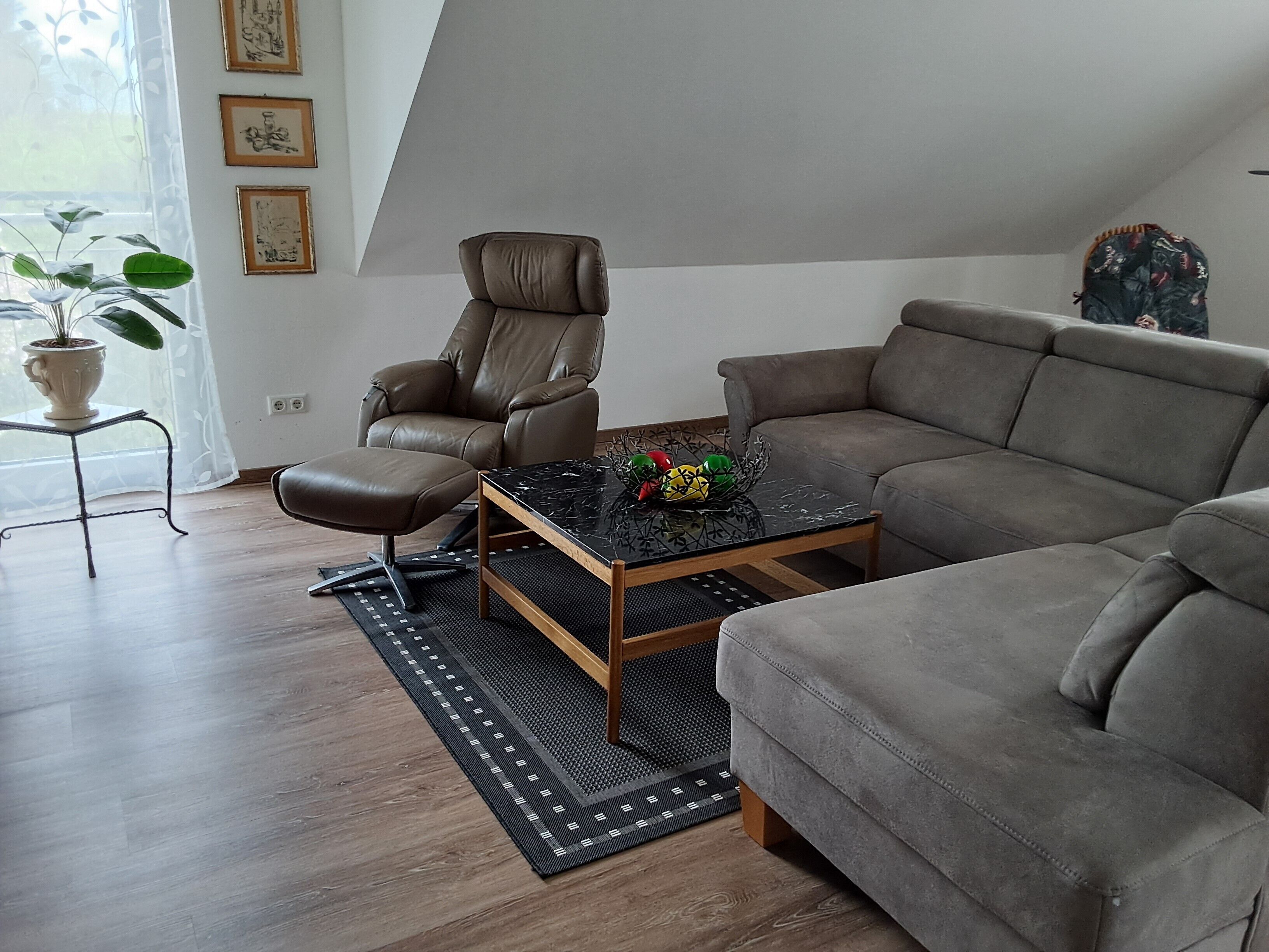En moderne stue med en læderlænestol, en sofa, et sofabord og en potteplante.