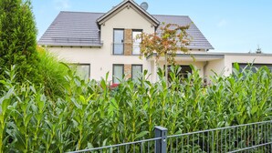 Une maison à deux étages, avec un toit gris, un balcon et une clôture en métal au premier plan.