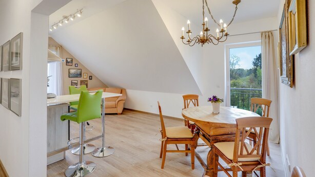 Un coin repas avec une table ronde en bois, des chaises, un lustre et une vue dégagée sur l’extérieur grâce à une grande fenêtre.