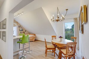 Un coin repas avec une table ronde en bois, des chaises, un lustre et une vue dégagée sur l’extérieur grâce à une grande fenêtre.