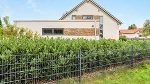 Une maison moderne à deux étages, dotée d’une façade en pierre, d’une clôture en métal à l’avant et surplombant un ciel dégagé.