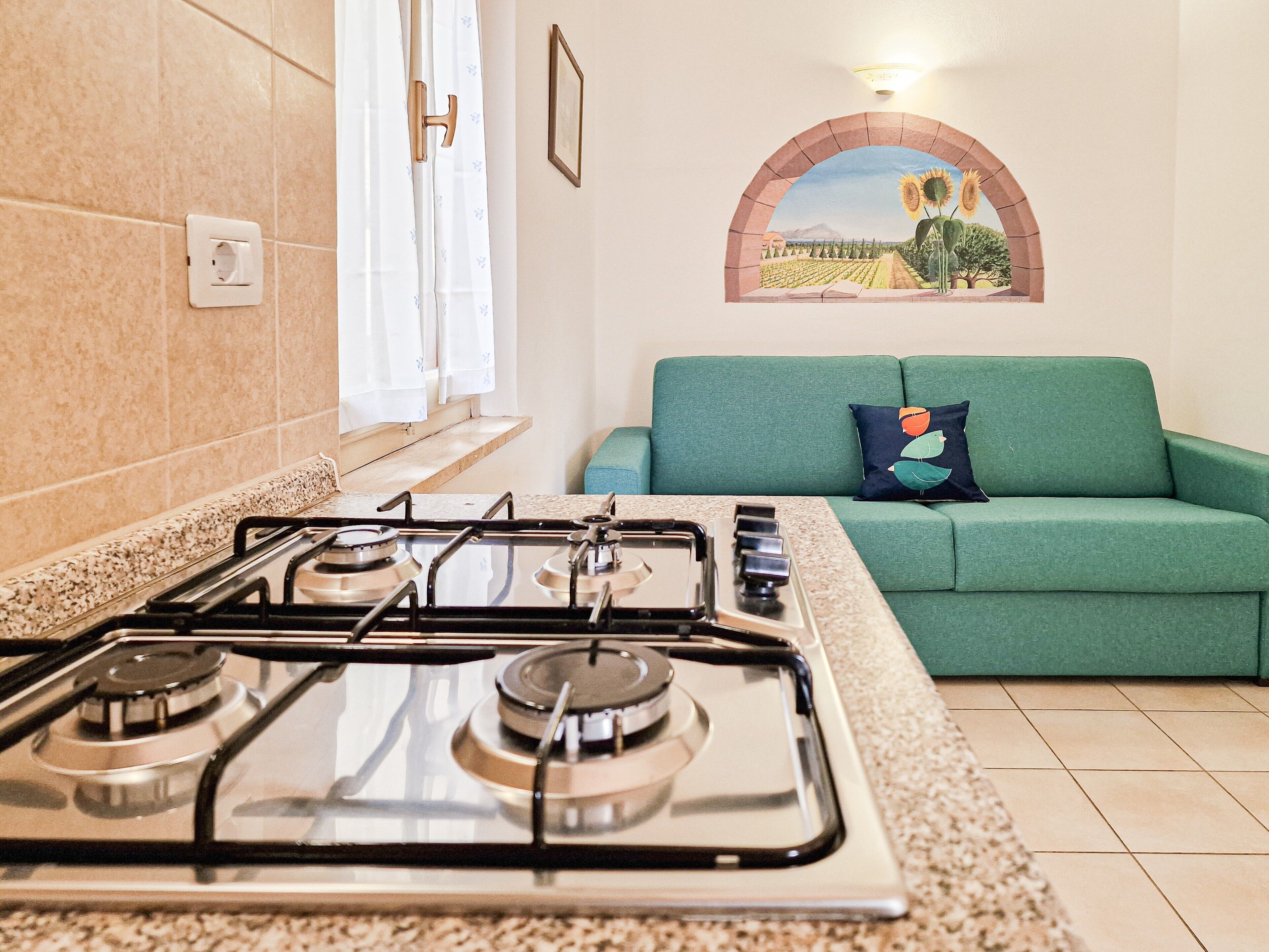 A kitchen with a gas stove, a green sofa, and a wall-mounted picture of a landscape.