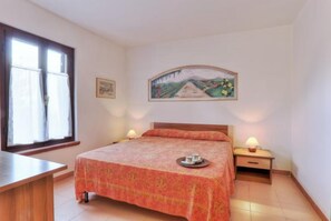 Une chambre à coucher avec un lit, deux tables de chevet, une fenêtre et un tableau au mur.