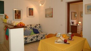 Un comedor con mantel amarillo, un sofá estampado con motivos florales y una encimera de cocina con frutas.