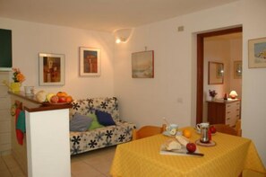 A dining area with a yellow tablecloth, a sofa with a floral pattern, and a kitchen counter with fruits.