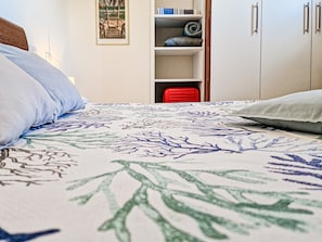A bedroom with a bed, pillows, a wardrobe, and a shelf with items.