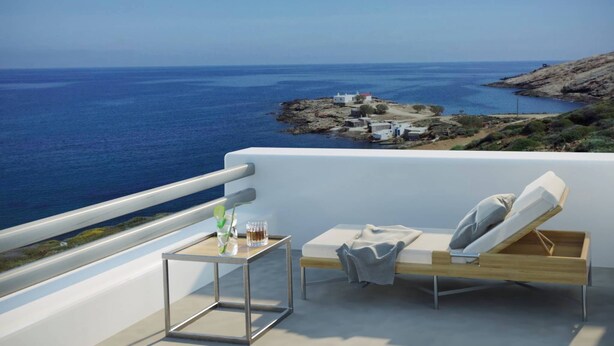Un balcón con vistas al mar, una pequeña mesa con una bebida y una silla de descanso.