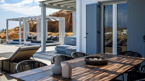 Un área de estar moderna al aire libre con una mesa de madera, sillas de mimbre y una pérgola blanca.