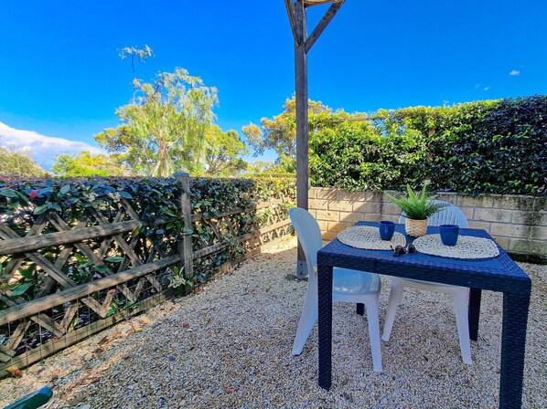 Une terrasse avec une table et des chaises, une clôture en bois et une haie.
