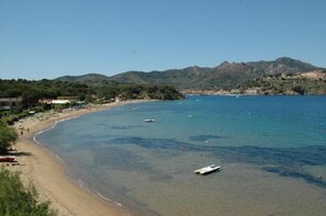 Une plage côtière avec une eau claire, des bateaux et une montagne en arrière-plan.