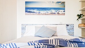 Una cama con una colcha a rayas, un cabecero con diseño pintado y un cuadro enmarcado de una playa en la pared.