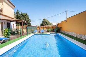 Une piscine avec deux chaises longues, un patio couvert et un mur en pierre.