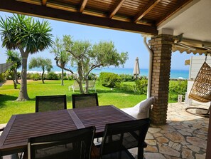 An outdoor patio with a table and chairs, overlooking a grassy area with trees and a view of the sea. - Corfu Glyfada Menigos Resort 5-8 (Corfu)