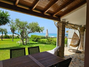 A covered outdoor seating area with a view of the sea, a hanging chair, and a table with chairs. - Corfu Glyfada Menigos Resort 5-8 (Corfu)