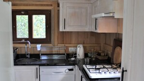 A compact kitchen with white cabinets, a dishwasher, a stove, and a window with a view of greenery.