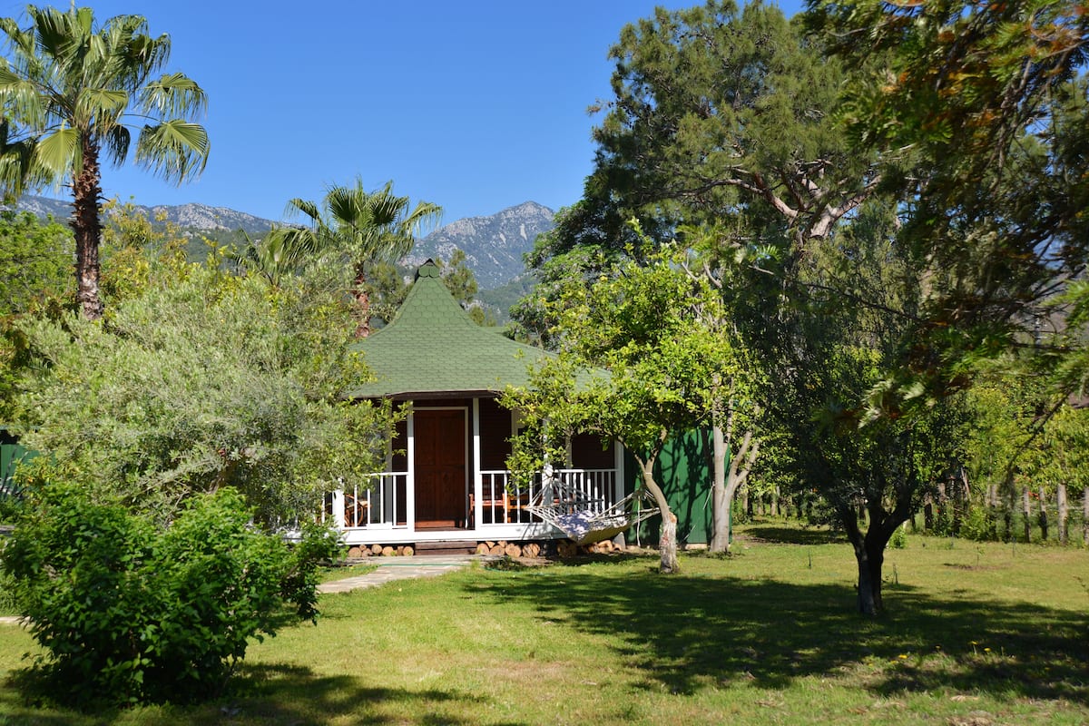 A house with a green roof, surrounded by trees and a mountain in the background.