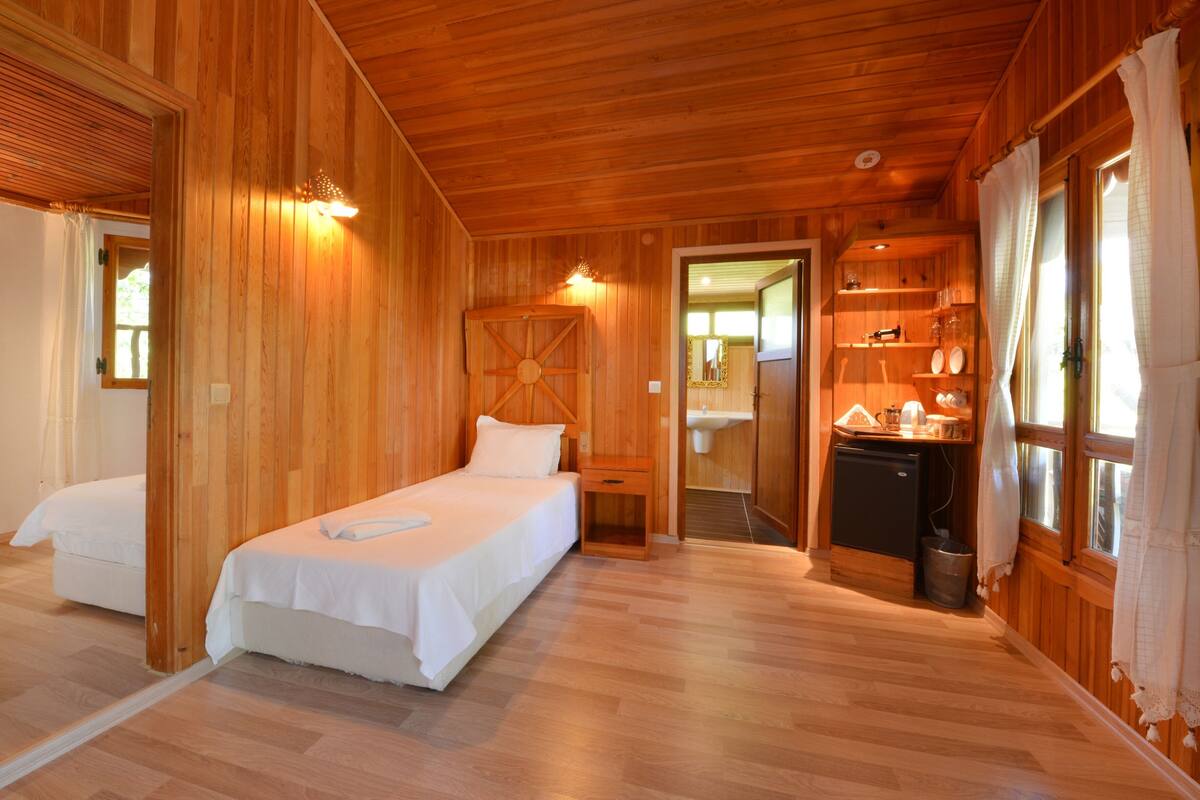 A wooden cabin with a bed, a small desk, and a kitchenette.