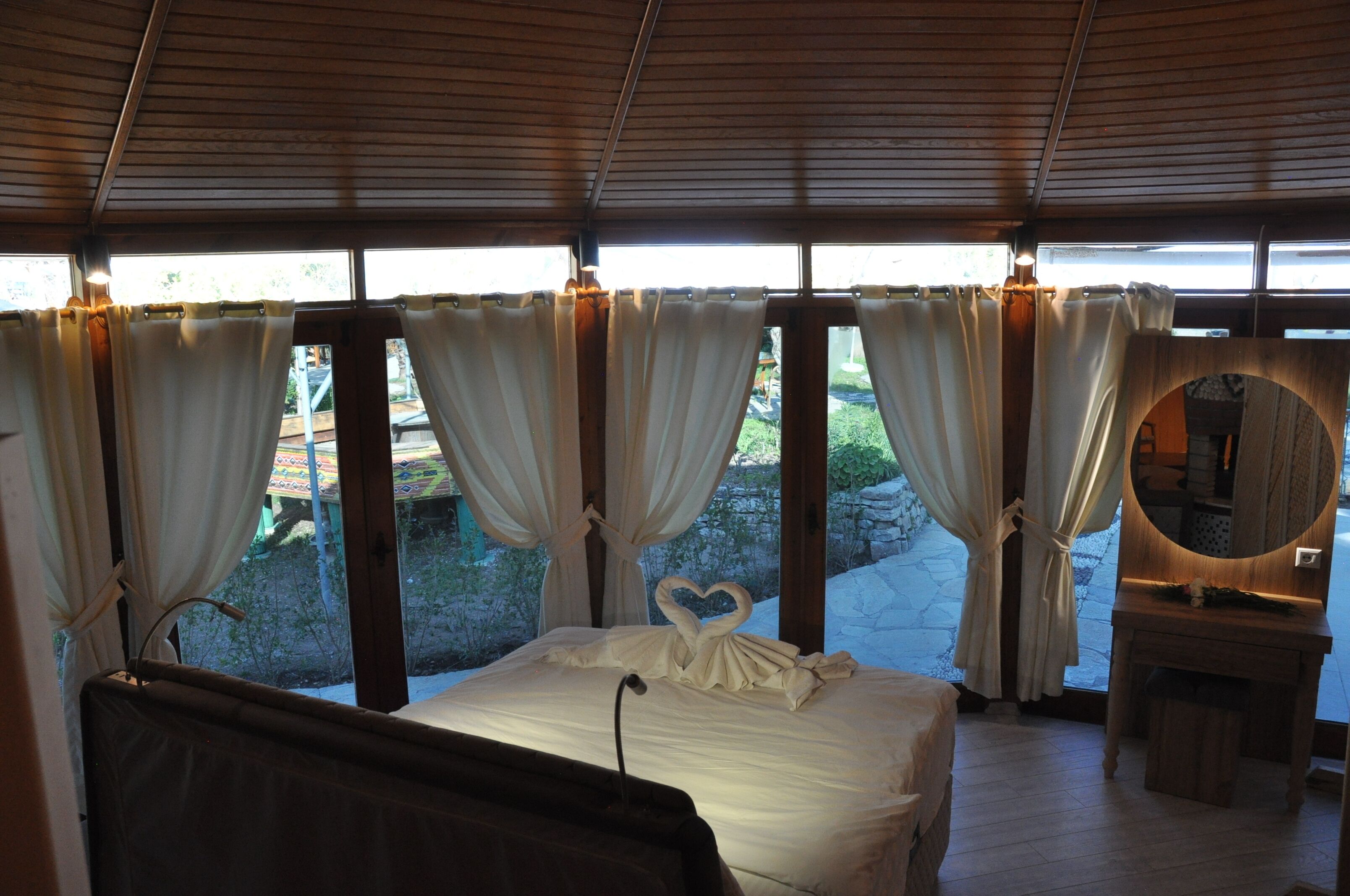 Un dormitorio con cama, cortinas, un espejo y vistas al exterior.
