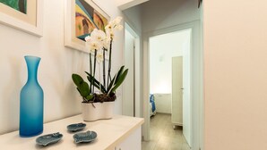 Un couloir avec un vase blanc et une plante orchidée, un vase bleu et une petite assiette posée sur un comptoir.