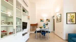 Un salon moderne comprenant un coin repas, des meubles blancs, un téléviseur et des œuvres d’art accrochées aux murs.