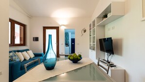 Un salon moderne avec une table à manger à plateau de verre, un vase bleu et un saladier rempli de fruits.