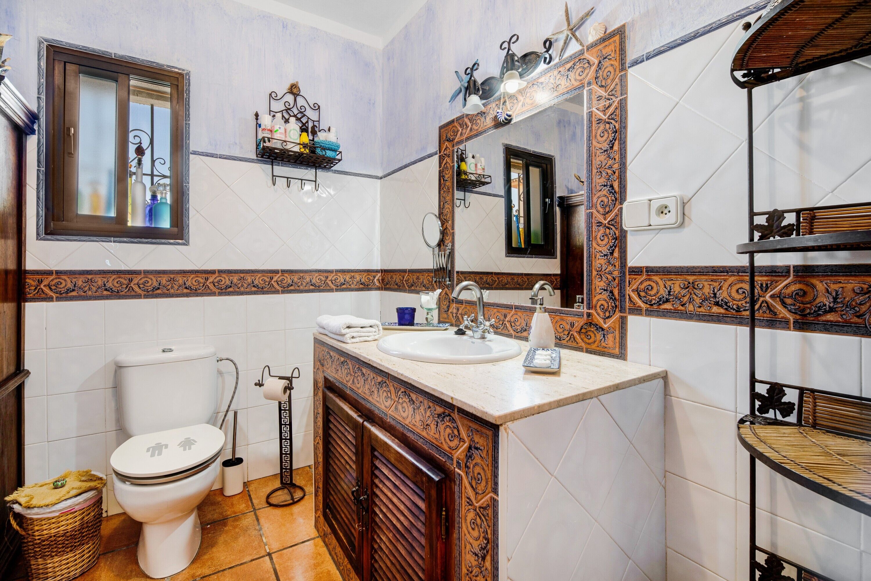 A bathroom with a toilet, sink, mirror, and decorative tiles.