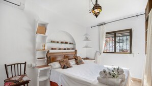 Ein Schlafzimmer mit einem Holzbett, weißen Wänden, einem Holzstuhl, einem Nachttisch, einer Lampe und einem Fenster mit Blick.
