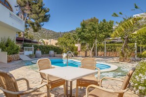 A pool area with wicker furniture, a stone patio, and a mountain backdrop.