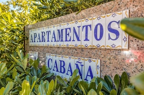 A sign with 'APARTAMENTOS' and 'CABANA' written on it, surrounded by greenery.