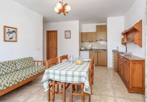 A compact living space with a dining table, chairs, a sofa, a kitchen area, and a ceiling light fixture.