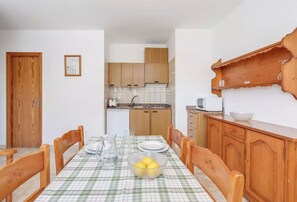 A dining area with a table set for four, wooden chairs, a checkered tablecloth, and a kitchen in the background.