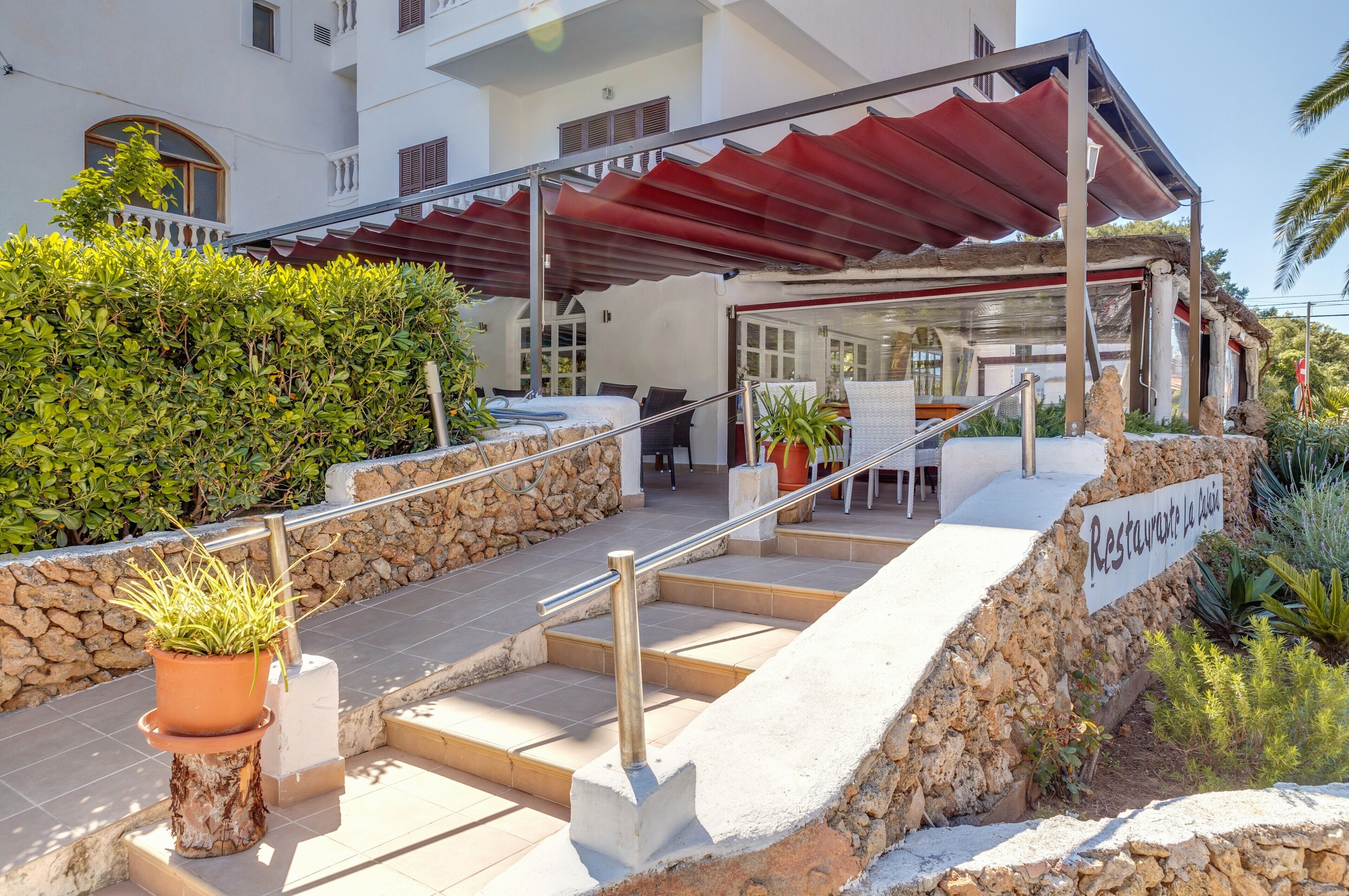 Ein Hotel mit Eingangsbereich, Steinstufen, einer Sitzgelegenheit im Freien und einer überdachten Terrasse.