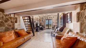 A spacious living area with leather sofas, a piano, and a staircase leading to an upper level.