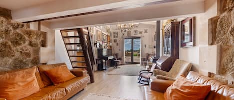 A spacious living area with leather sofas, a piano, and a staircase leading to an upper level.