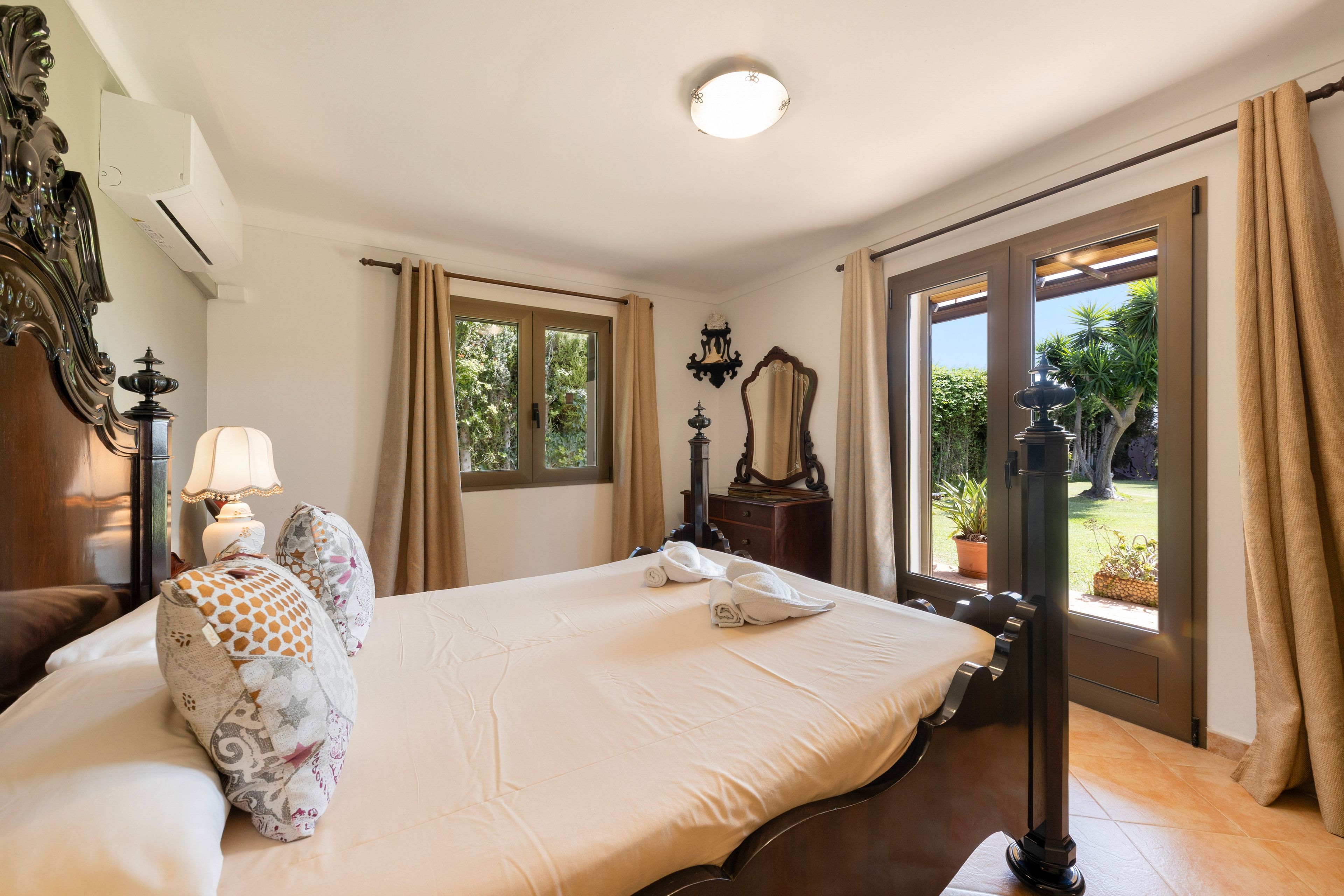 Habitación de hotel con cama, mesita de noche, lámpara, espejo y vista al exterior.