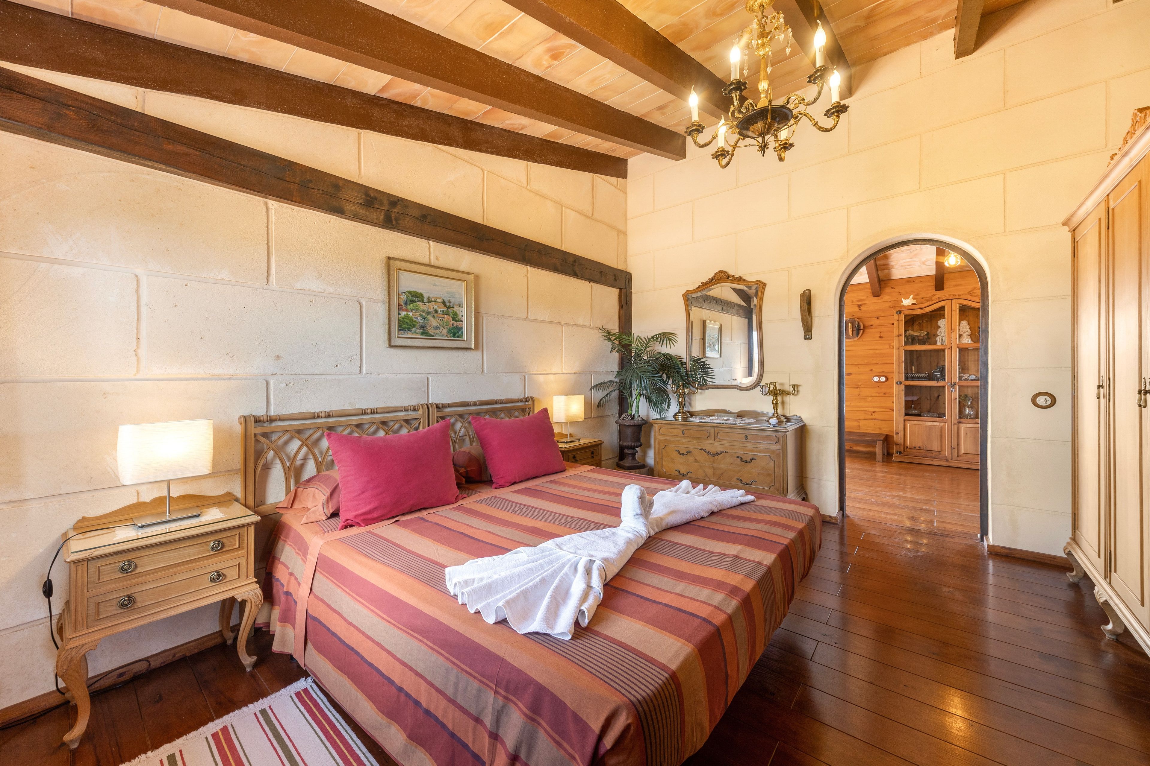 Habitación de hotel con techo de madera, cama con ropa de cama a rayas, mesita de noche, cómoda y espejo.