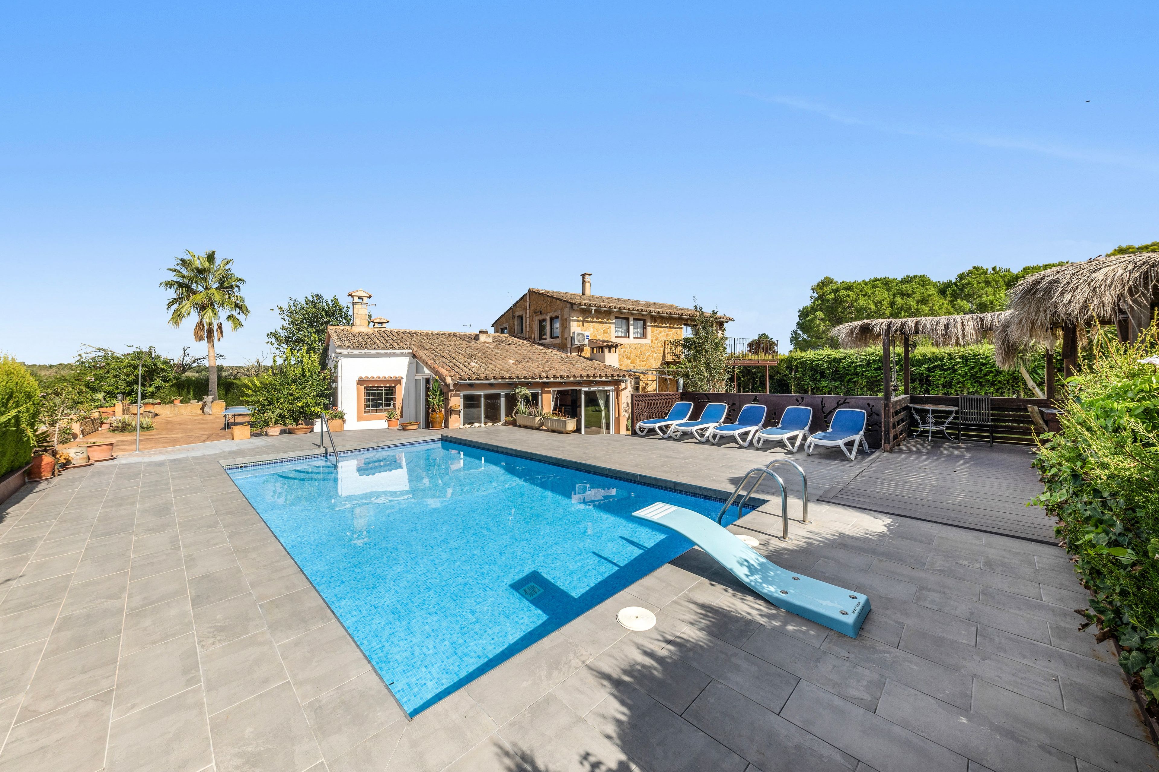 A swimming pool with a tiled deck, lounge chairs, and a building with a tiled roof.