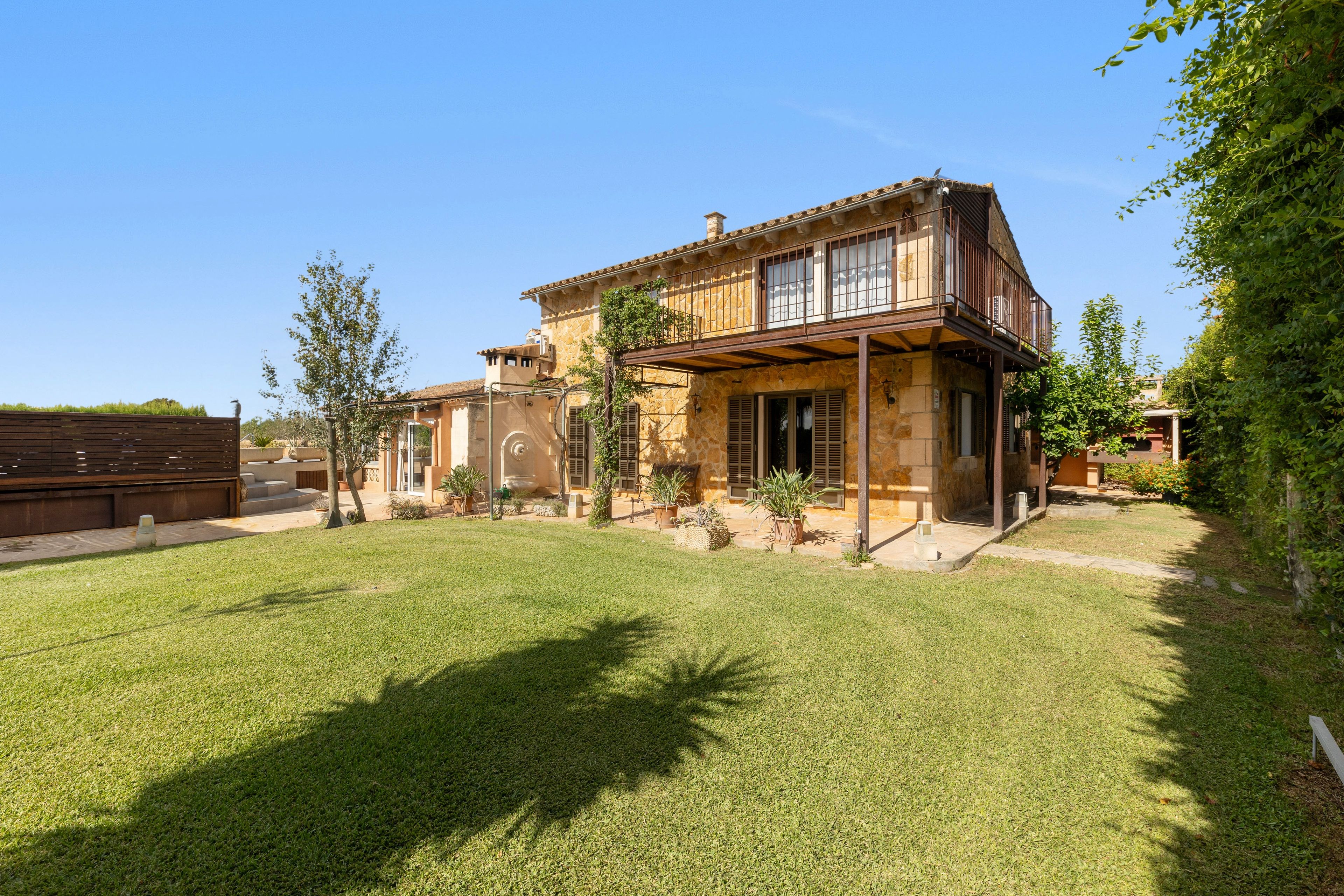 A two-story stone house with a covered patio and a well-maintained lawn.