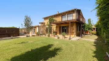 A two-story stone house with a covered patio and a well-maintained lawn.