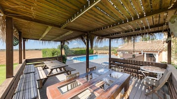 Eine überdachte Terrasse im Freien mit Holzmöbeln, einem Schwimmbad und Blick auf die Landschaft.
