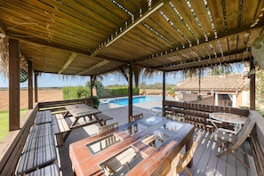 An outdoor covered patio with wooden furniture, a swimming pool, and a view of the countryside.