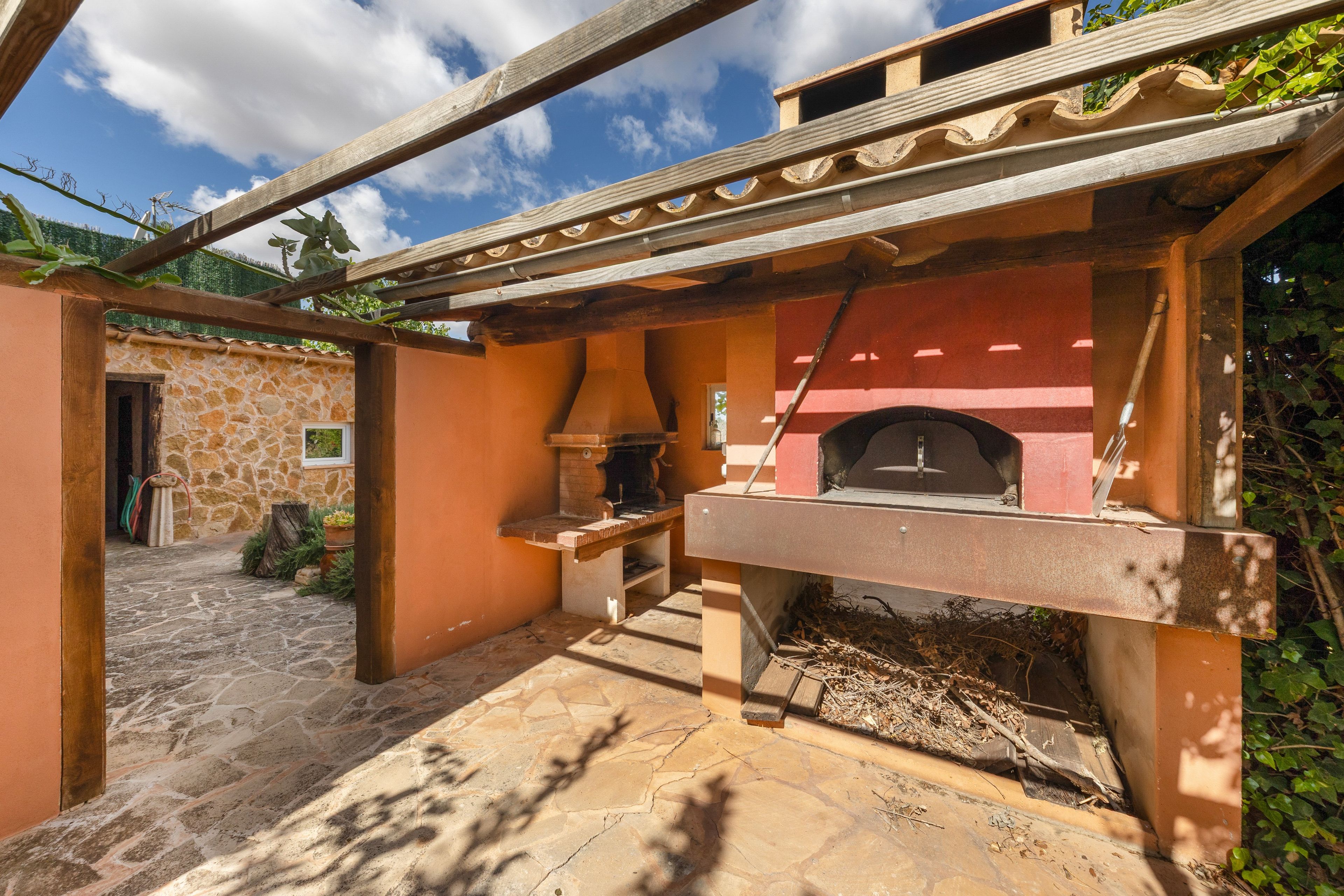 Un bâtiment en pierre doté d’un four en briques, d’une pergola en bois et d’un chemin en pierre.