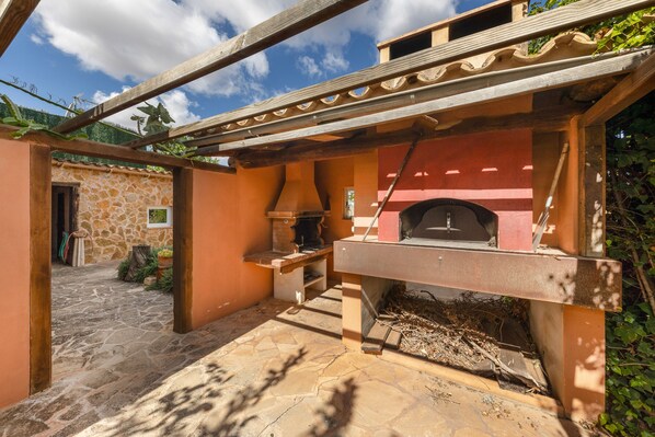 A stone building with a brick oven, a wooden pergola, and a stone pathway.