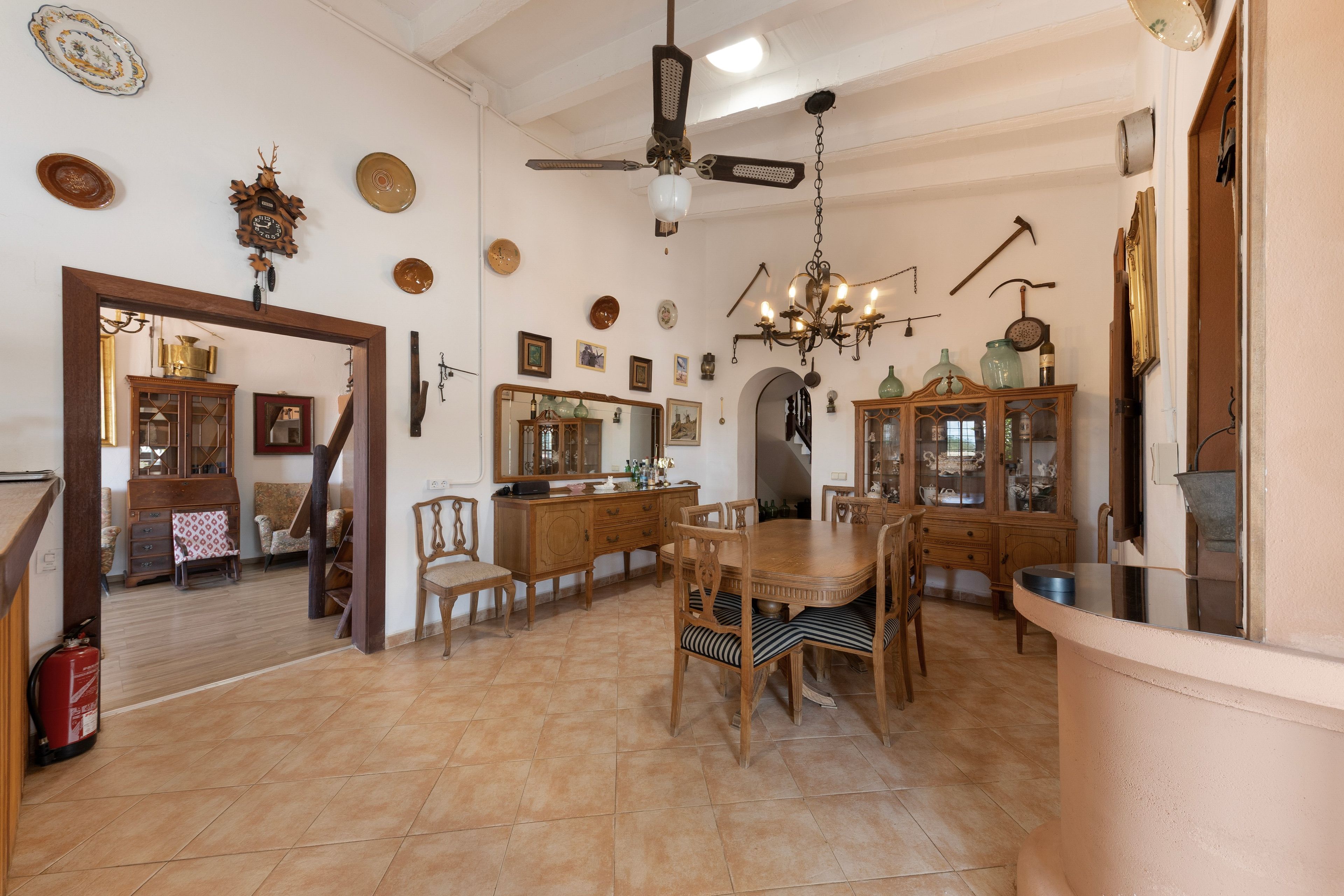 Un comedor amplio con una mesa y sillas de madera, una araña y varios objetos decorativos en las paredes.