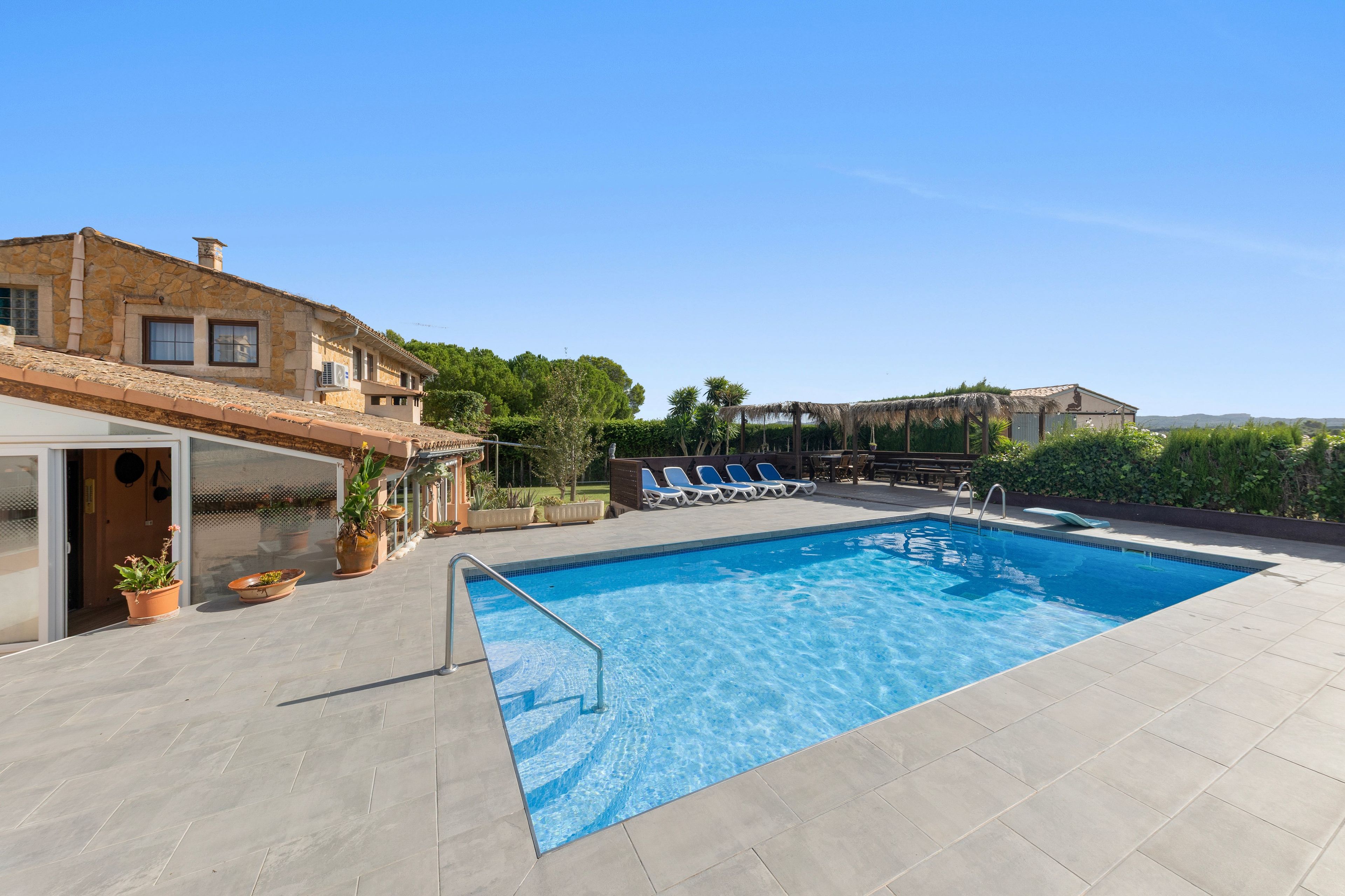 Une piscine avec une terrasse carrelée, des chaises longues et un bâtiment aux murs en pierre.