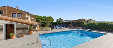 A swimming pool with a tiled deck, lounge chairs, and a building with stone walls.