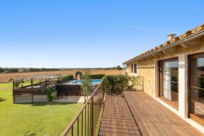 A wooden deck with a pool, a stone building with large windows, and a view of a field. - Spacious Mallorcan Villa “Es Rafal Nostro 11” with Pool (Felanitx)
