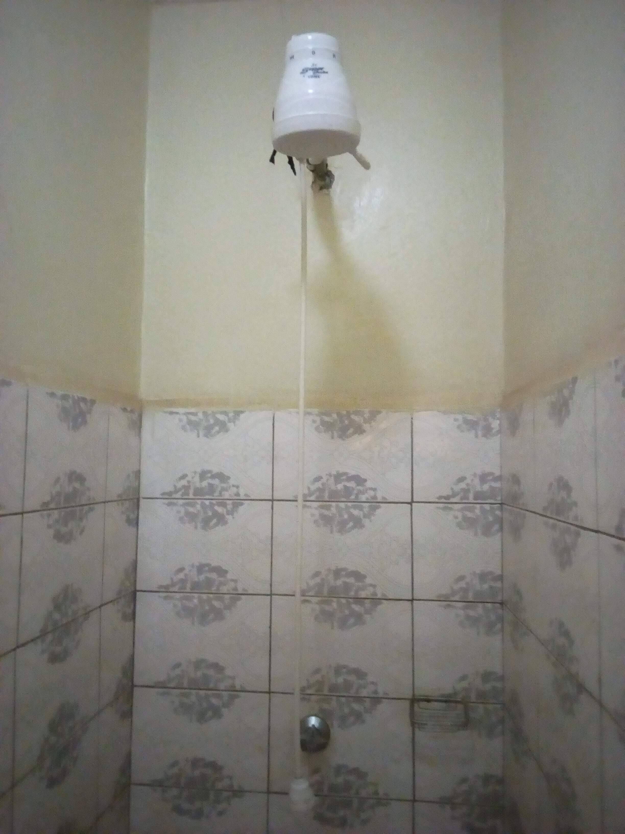 A bathroom with a shower head mounted on the wall, tiled with a floral pattern.