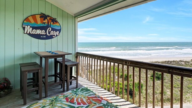 Un balcon avec vue sur l ’océan, une table avec des chaises et une pancarte indiquant « Mama Caye ».